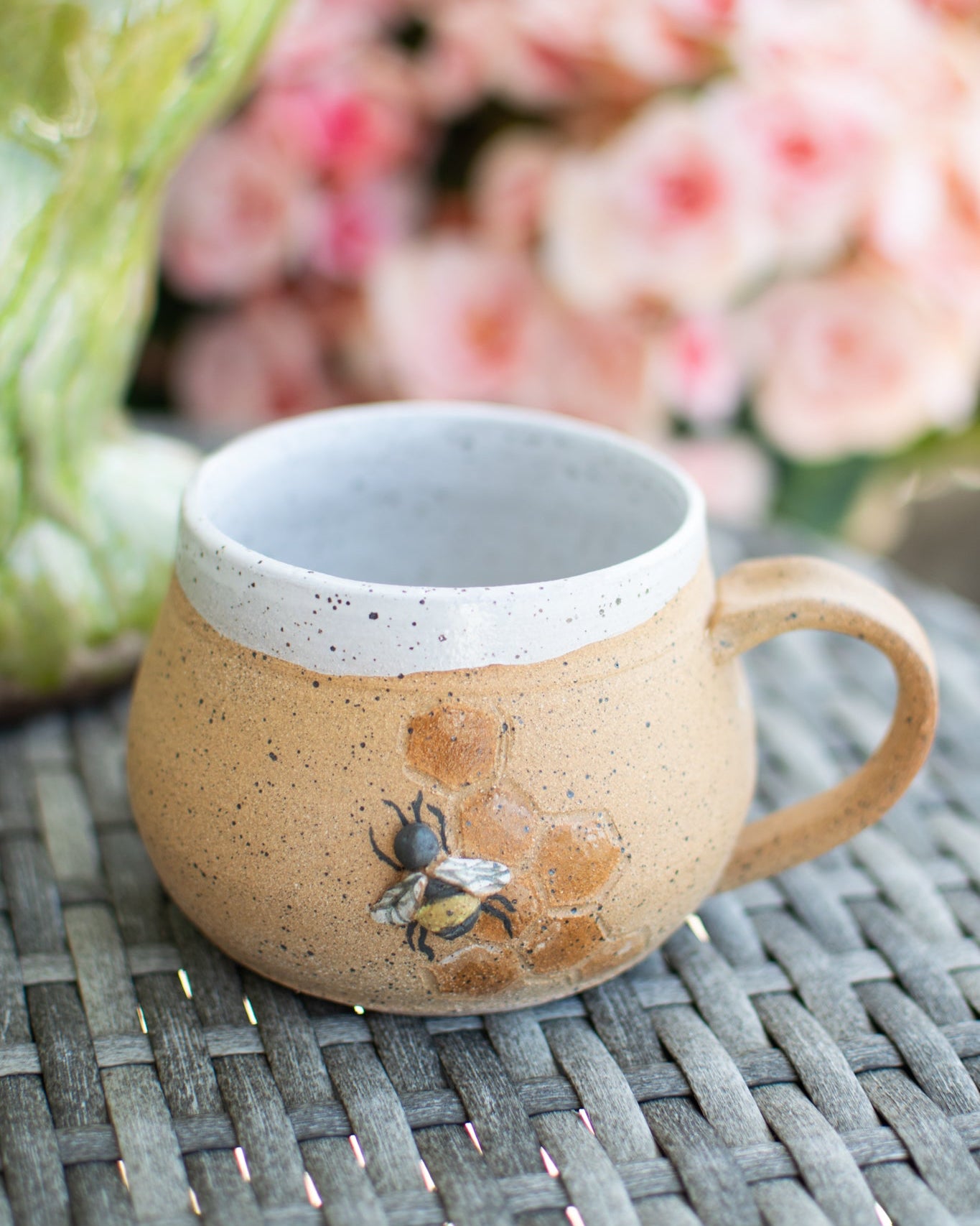 Two ceramic mugs with bee designs on a woven surface.