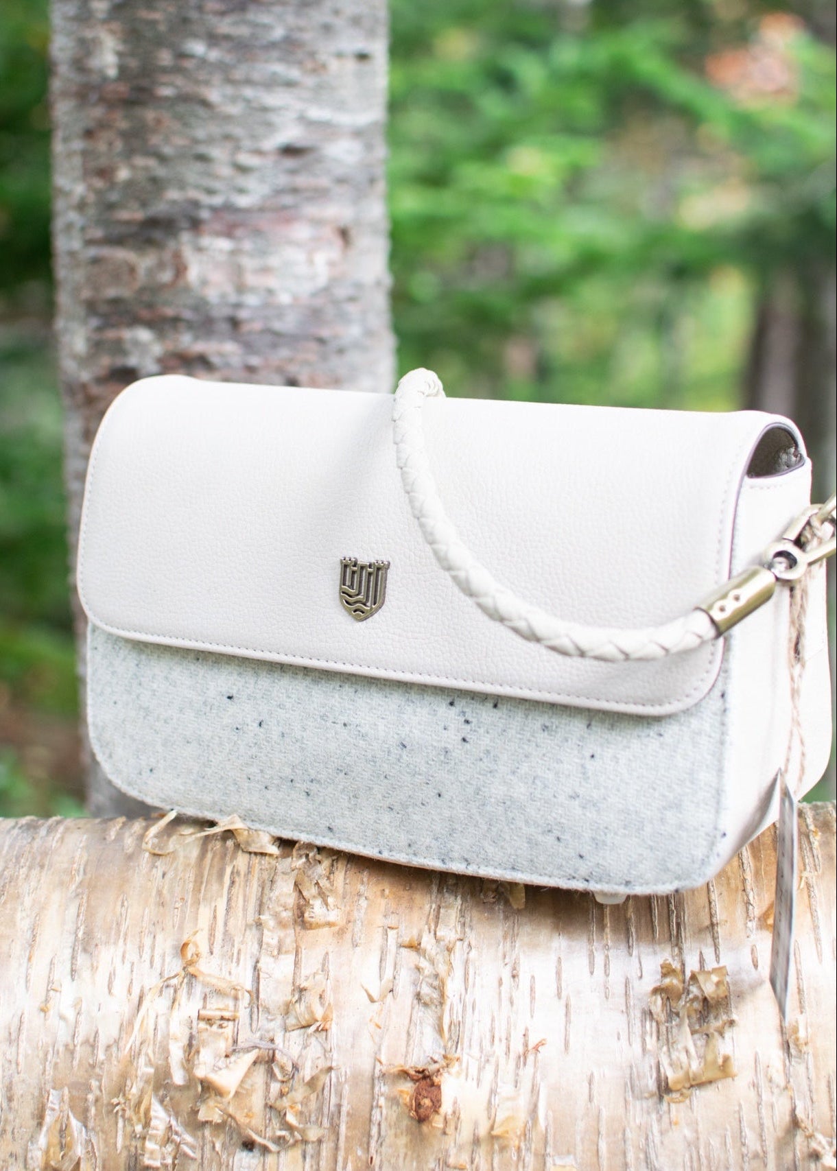 White handbag with a brand logo on a tree branch in a forest setting