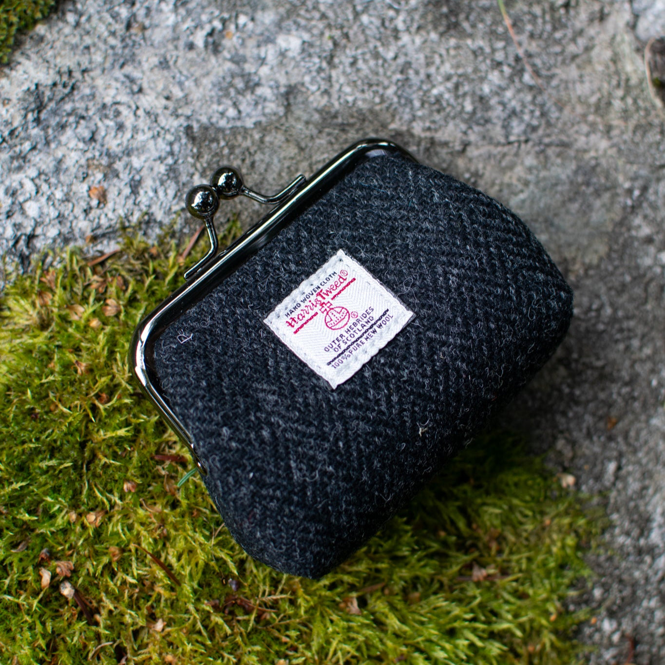 Black fabric pouch with a label on a stone surface with green moss.