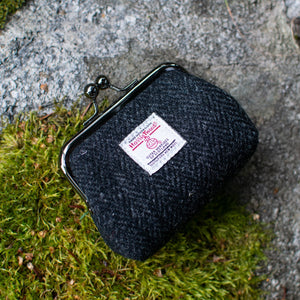 Black fabric pouch with a label on a stone surface with green moss.