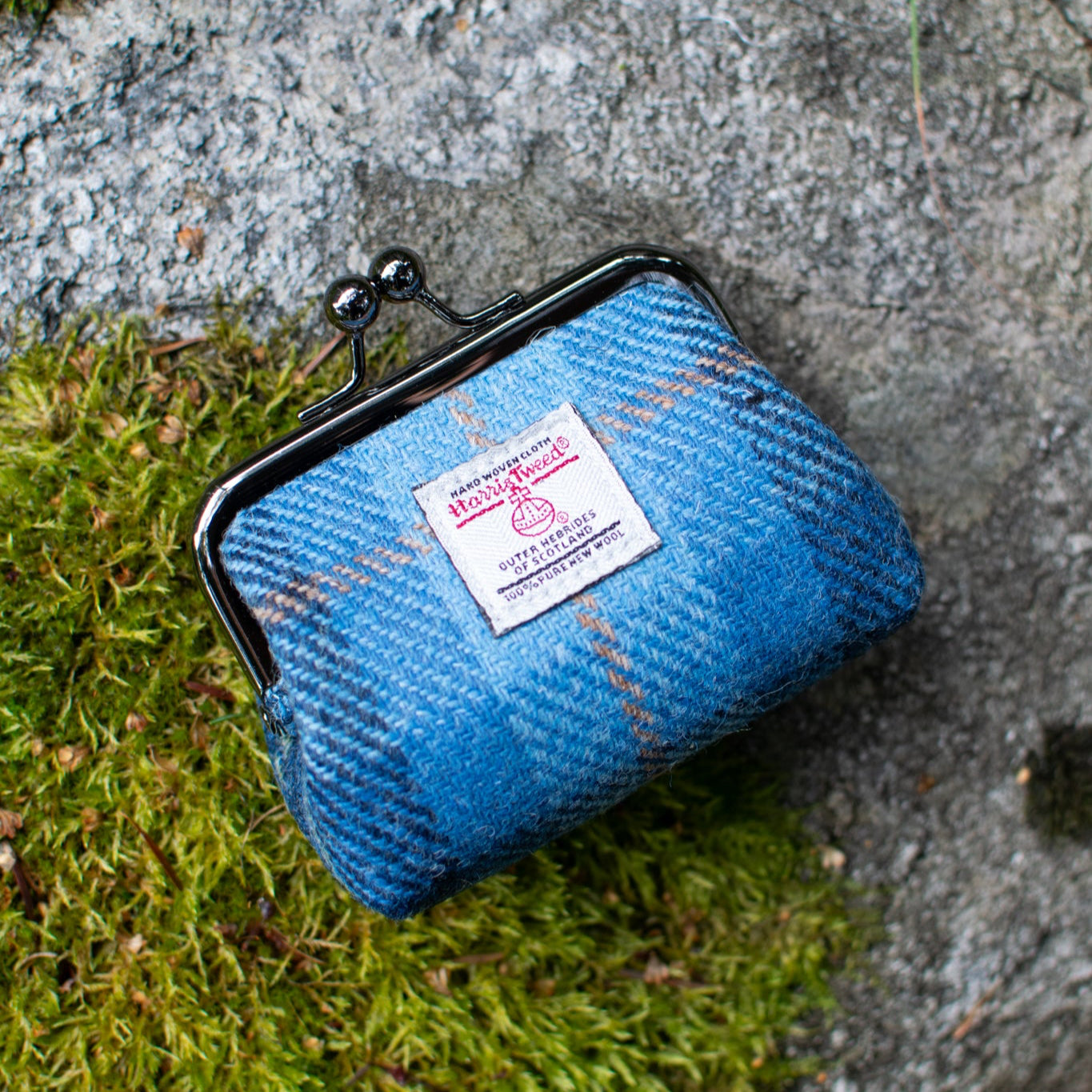 Blue fabric pouch with a brand label on a stone surface with moss