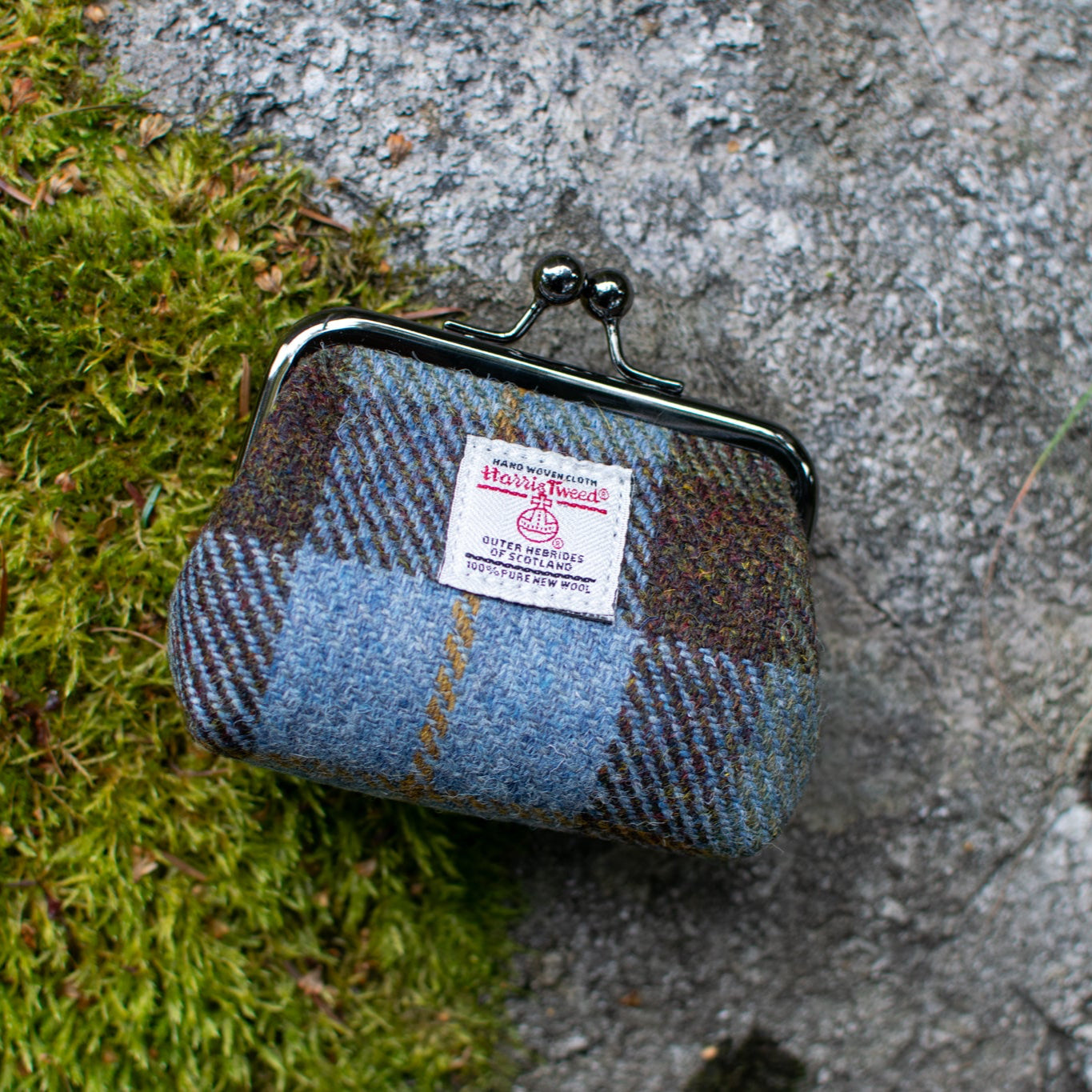 Plaid coin purse on a textured surface with a visible brand label