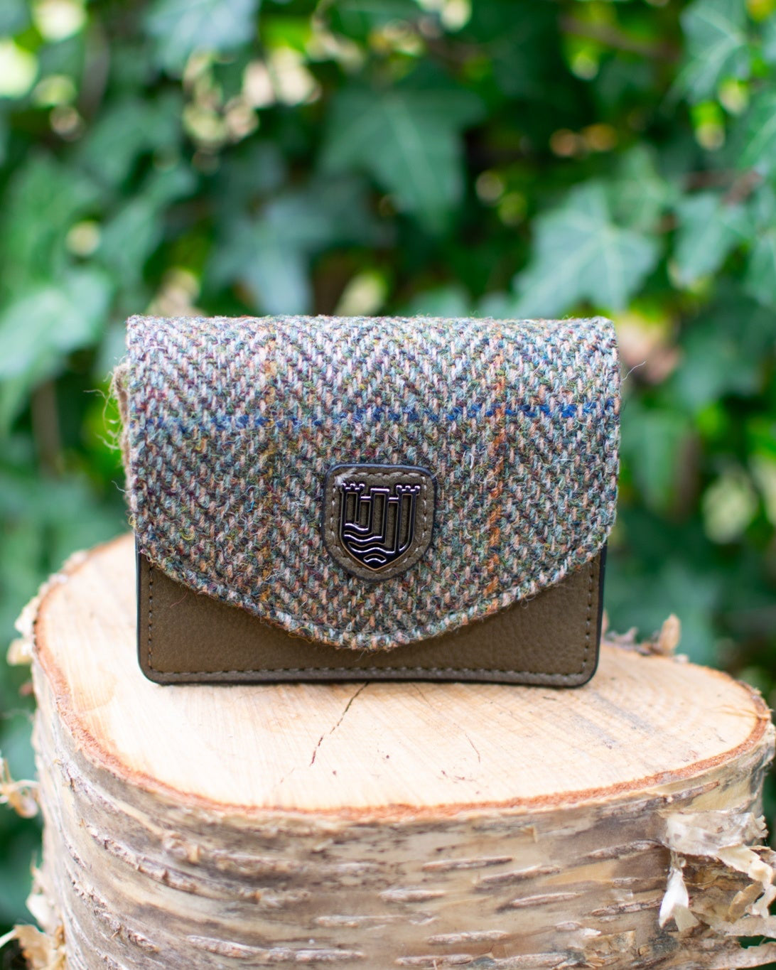 Herringbone patterned wallet on a wooden stump with green foliage in the background