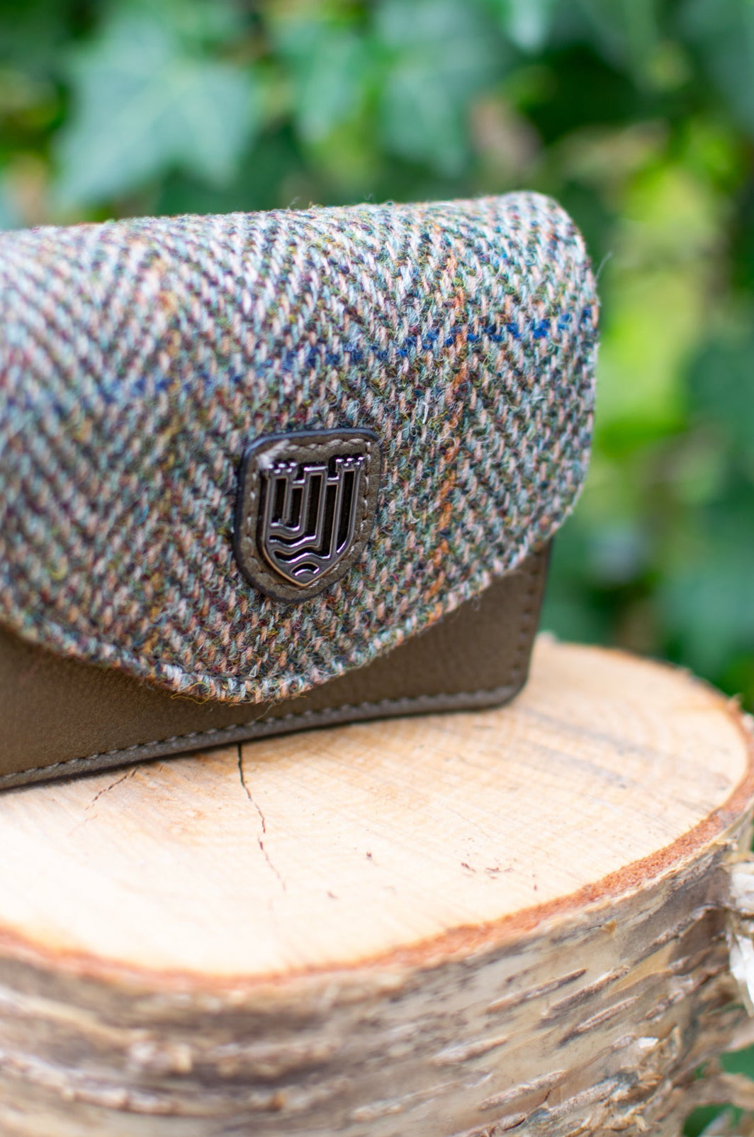 Herringbone patterned wallet on a wooden stump with green foliage in the background
