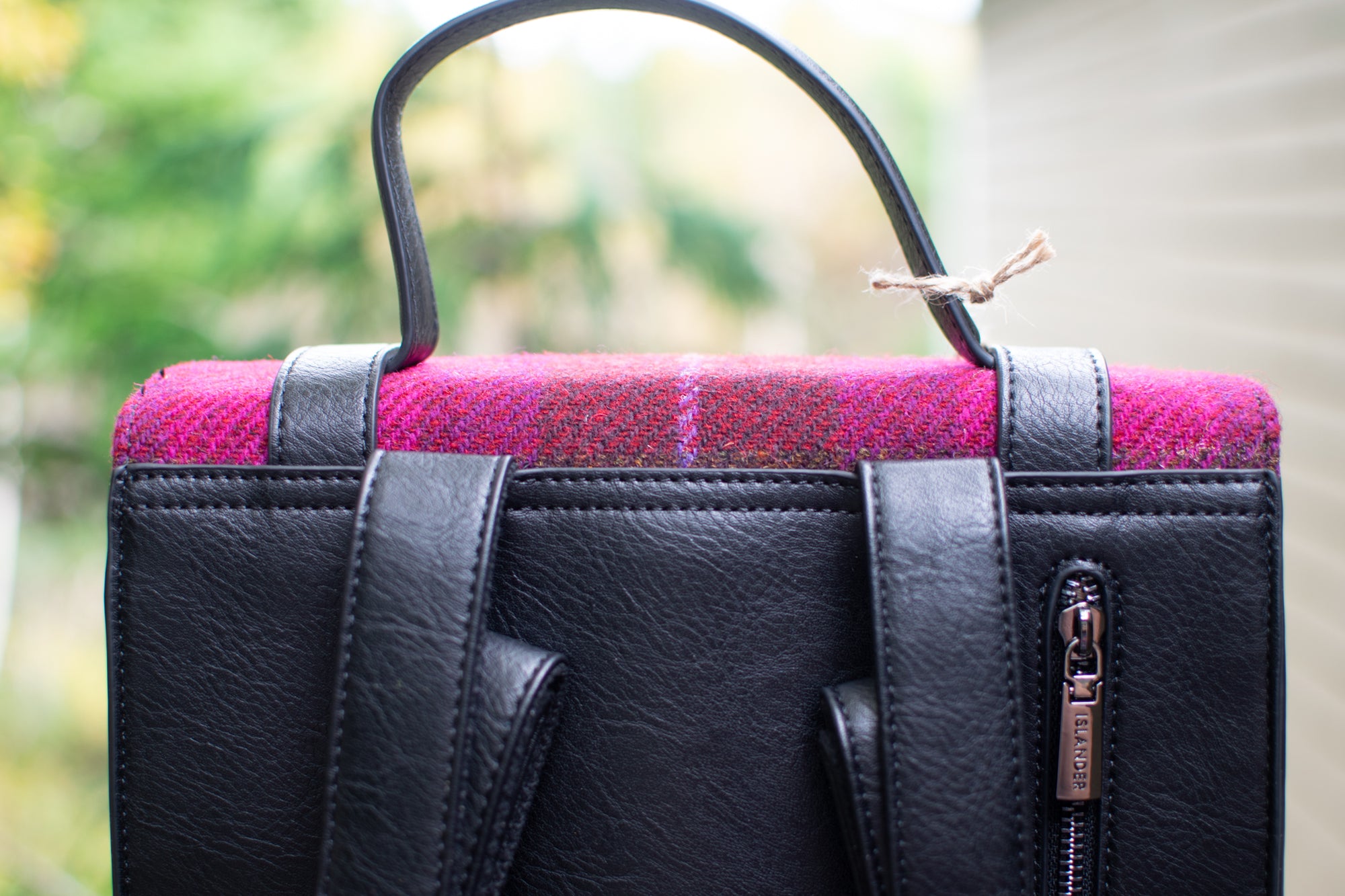 Black handbag with pink plaid pattern on a blurred natural background