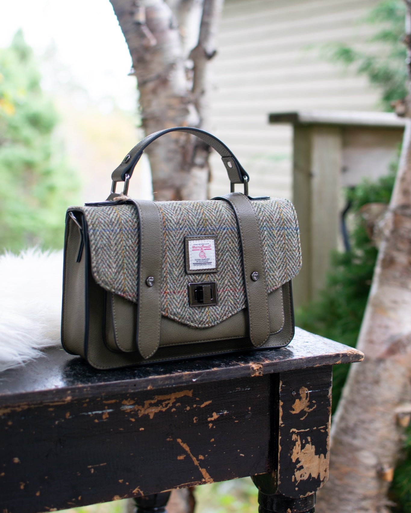 Green handbag on a rustic wooden table with blurred outdoor background