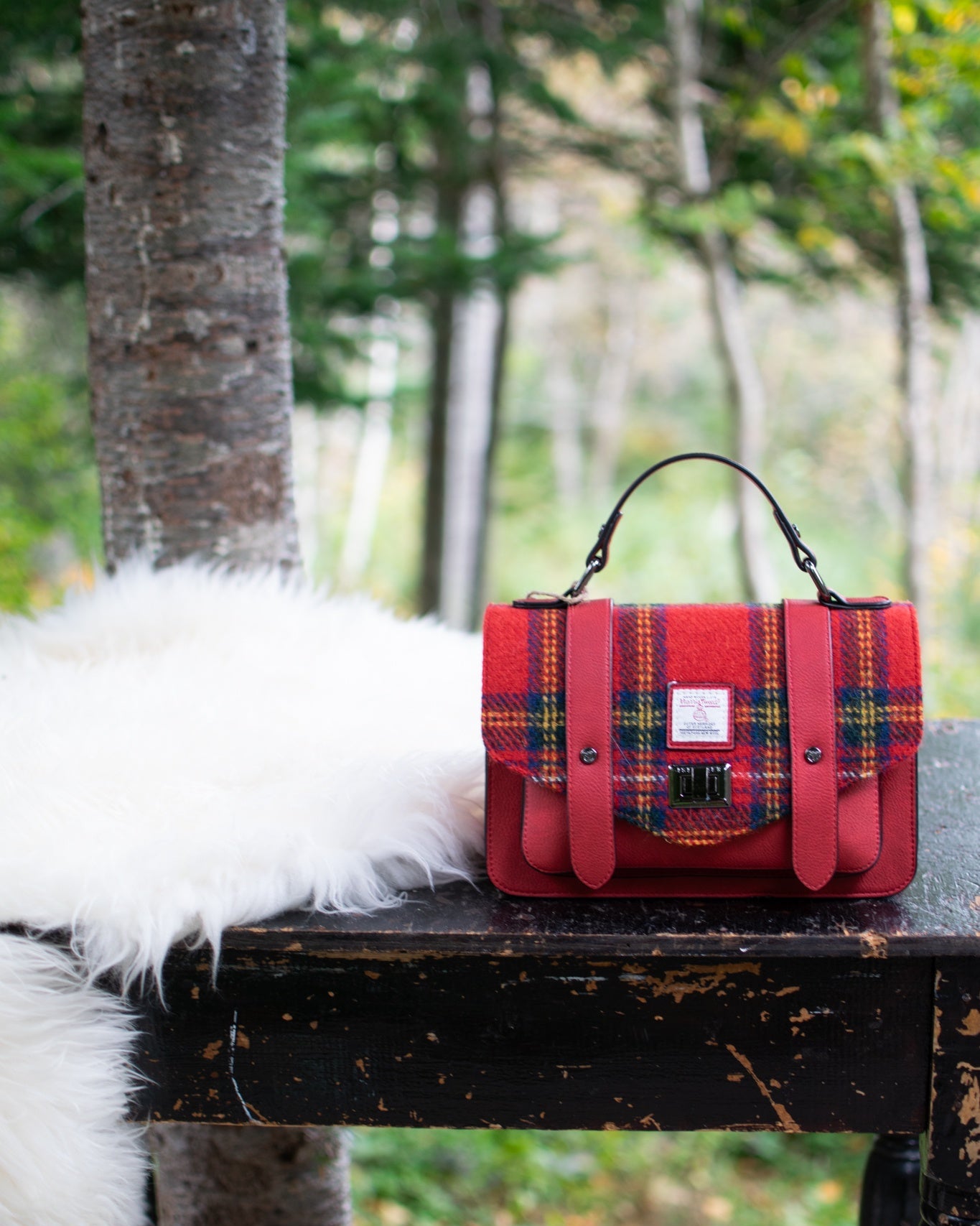 Red plaid handbag on a wooden table with a forest background