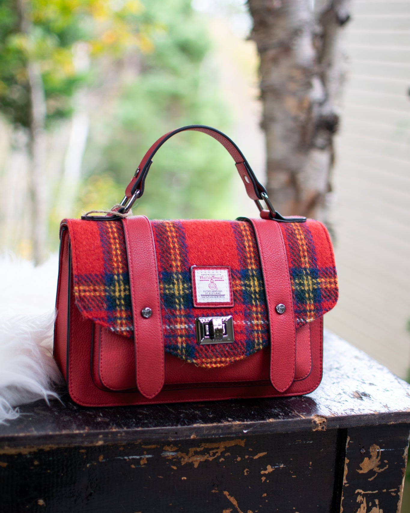 Red plaid handbag on a wooden table with a forest background