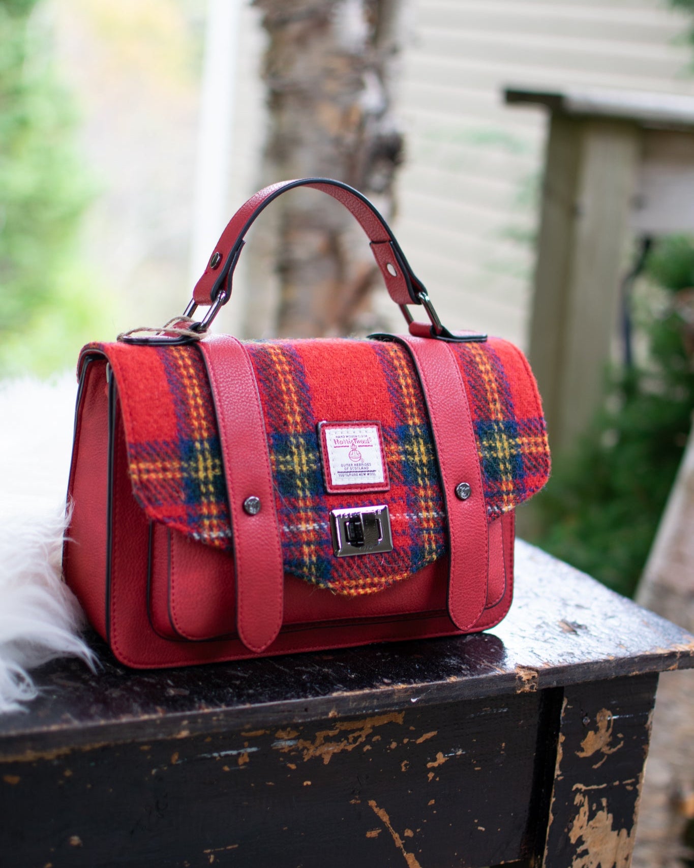 Red plaid handbag on a wooden surface with a blurred natural background