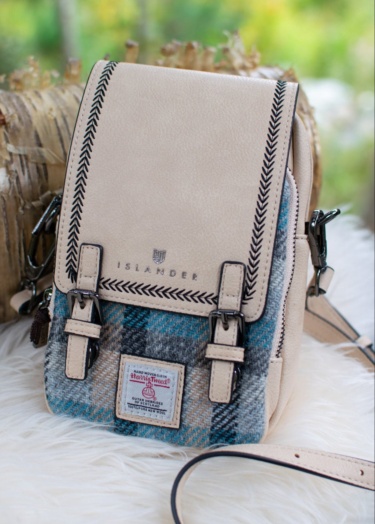 Crossbody bag with plaid pattern and beige top section on a fluffy white surface with blurred natural background