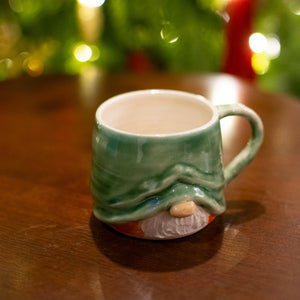 Green mug shaped like a gnome with a blurred Christmas tree in the background